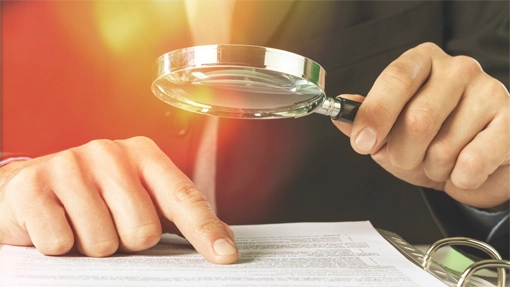 Magnifying glass on contract with hand scanning document.